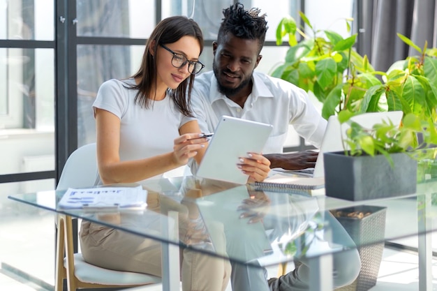 A financial advisor sitting across a table from a couple, pointing at a tablet displaying Social Security benefit projection charts. The setting is a well-lit and professional office environment.